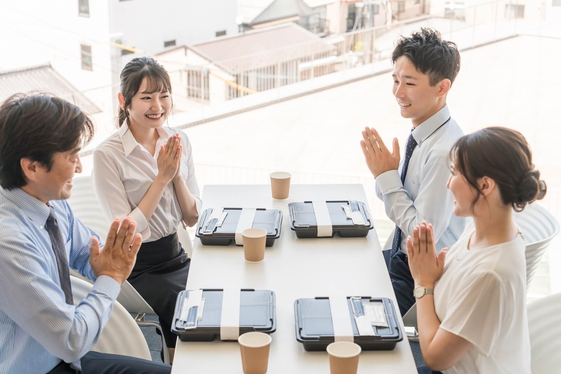 風通しの良い職場でランチタイムに和やかに談笑する上司と部下の4人。活発なコミュニケーションと笑顔。